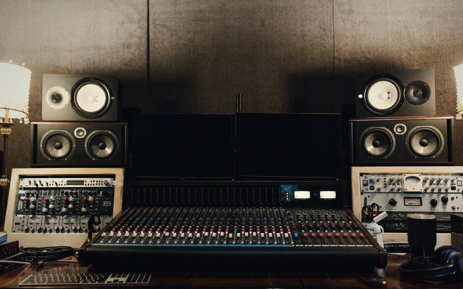 Recording studio mixing console flanked by studio monitors and dual computer screens